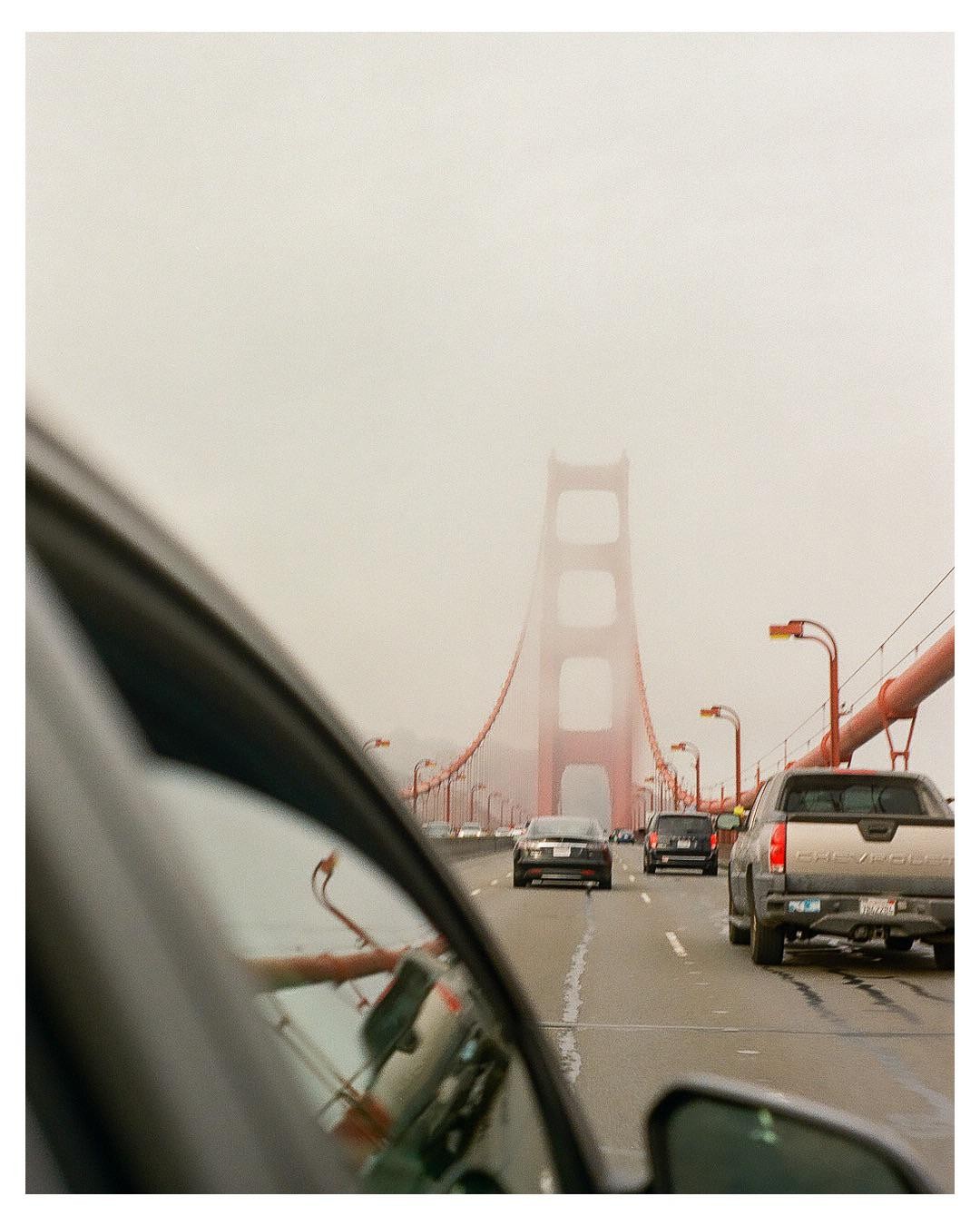 A red bridge is visible through a car window on a foggy day with other cars on the road.