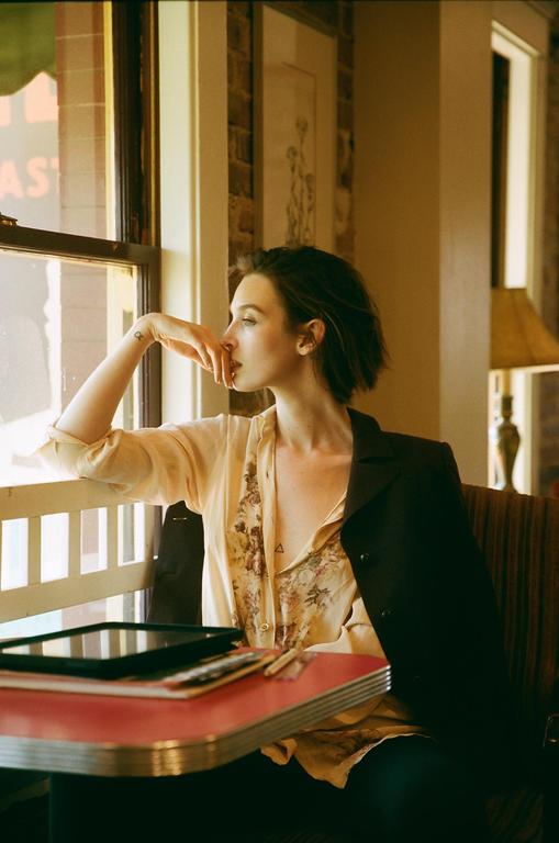 A woman with short hair looks out a window while sitting at a table with a tablet.