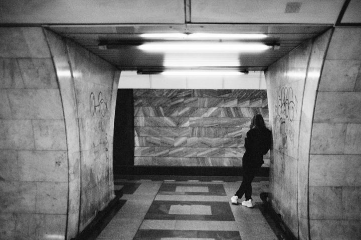 A person stands in a tiled underpass with fluorescent lights overhead.