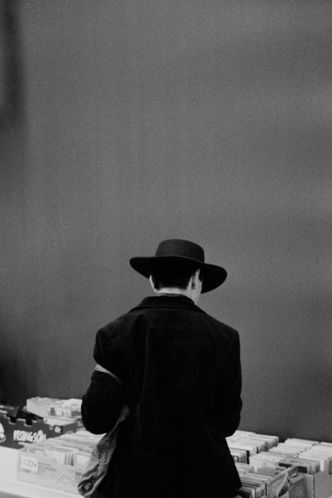 A man in a hat stands with his back to the viewer, looking at records.