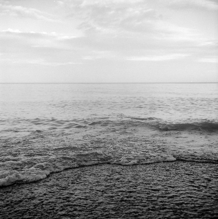 Waves break on a beach under a cloudy sky.