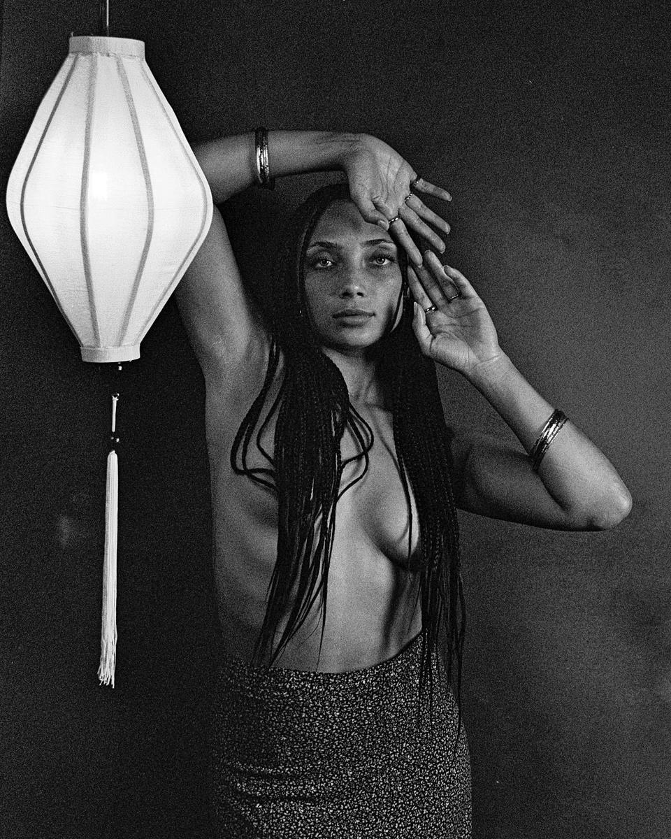 A woman with long braids poses next to a hanging lantern.
