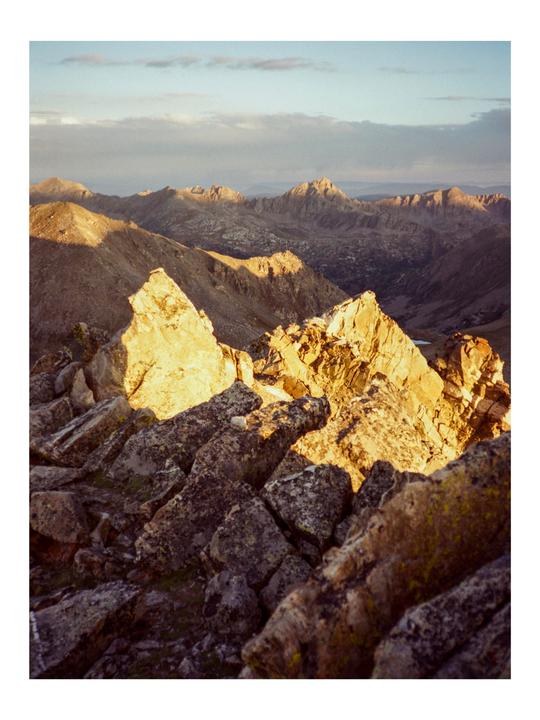 A mountain landscape is illuminated by the golden light of the setting sun.