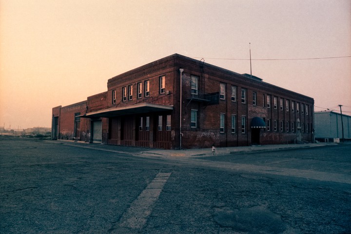 A large brick building with many windows stands at a street corner under a pale sky.