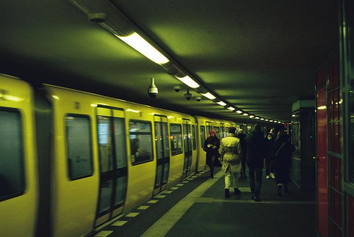 A yellow subway train is stopped at a station platform with people walking along the platform.
