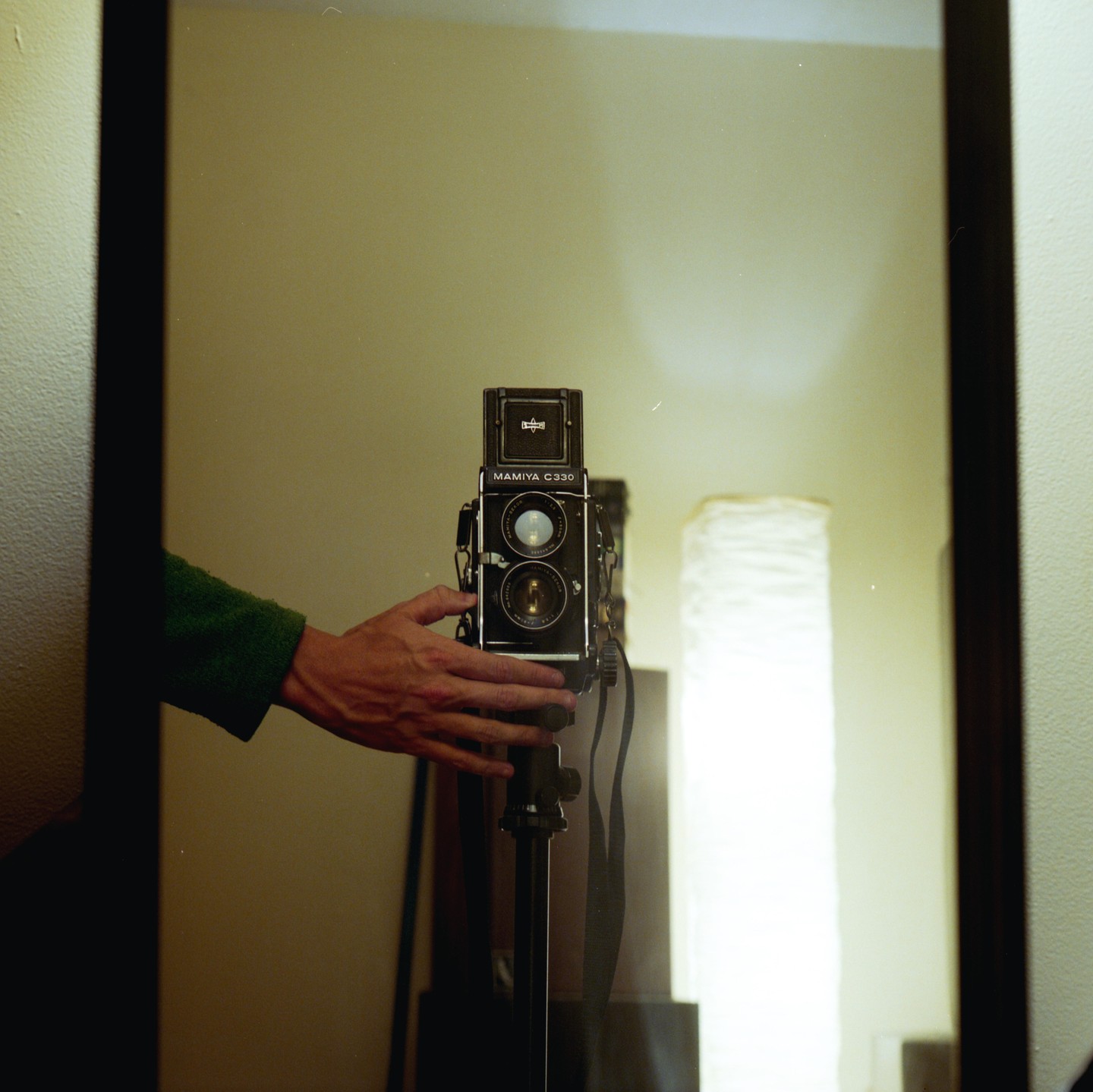 A hand holds a camera on a tripod, reflected in a mirror.
