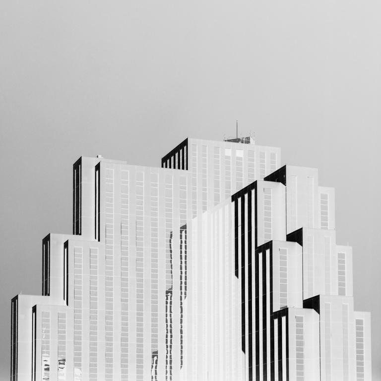A black and white photograph shows the top of a skyscraper with a stepped design.