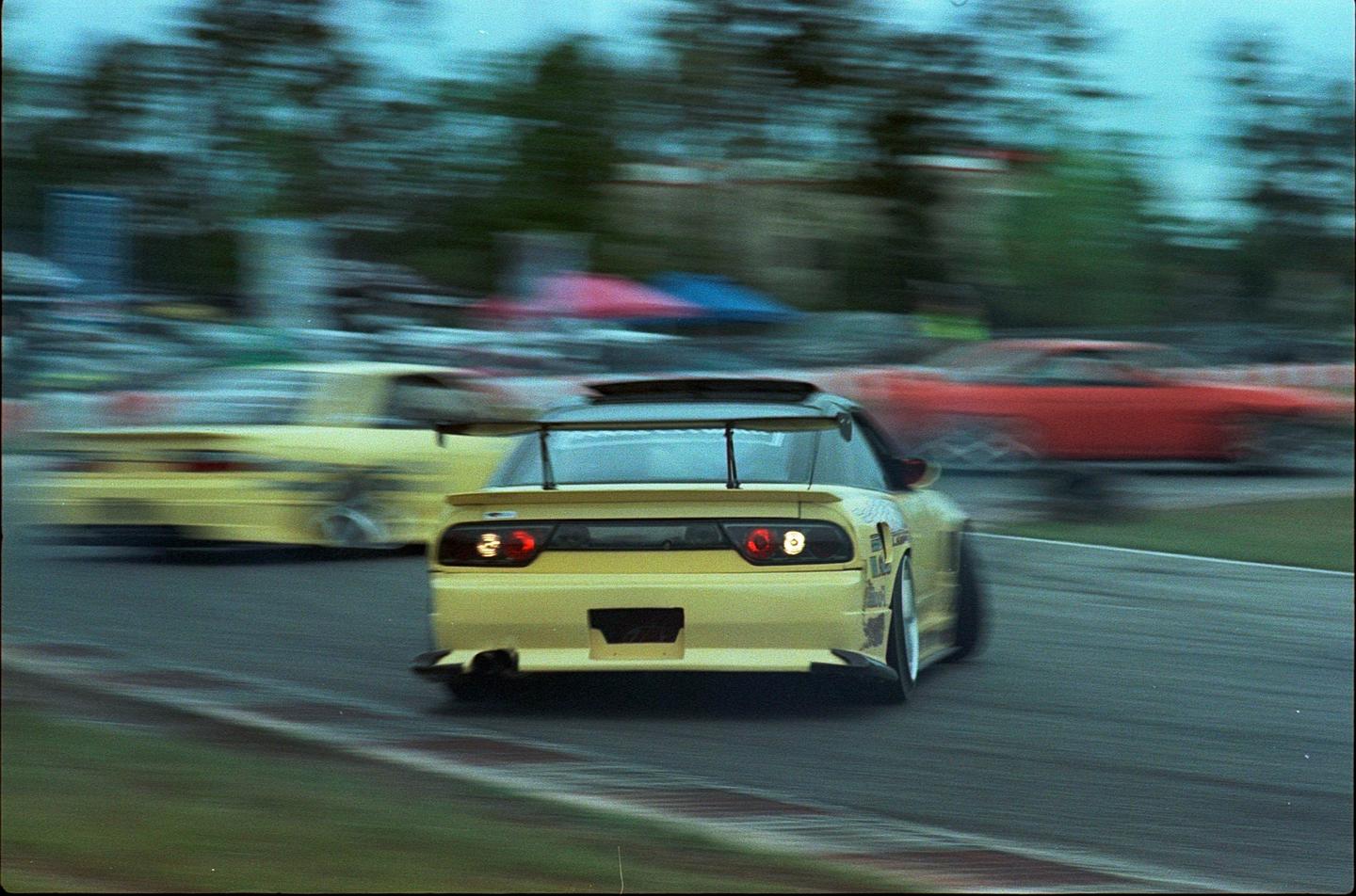 A yellow race car with a large spoiler speeds around a track, blurring the background.