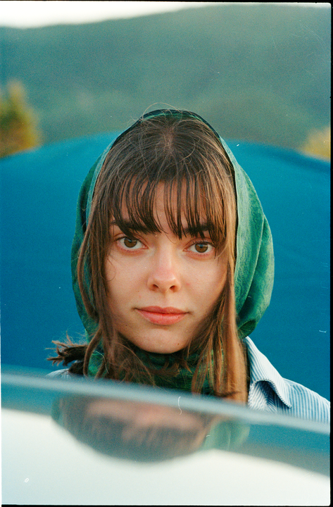 A woman wearing a green headscarf and a striped shirt looks directly at the viewer.