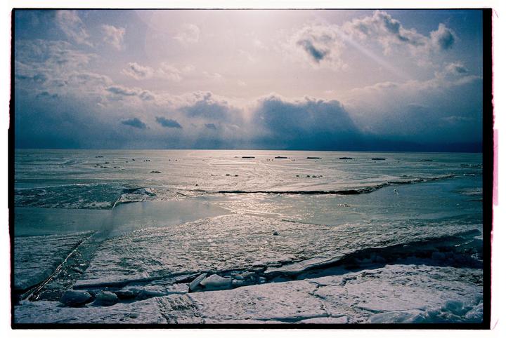 A vast expanse of frozen water with broken ice sheets stretches under a cloudy sky.