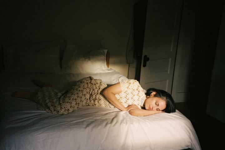 A woman sleeps on a bed in a dimly lit room, illuminated by a shaft of light.