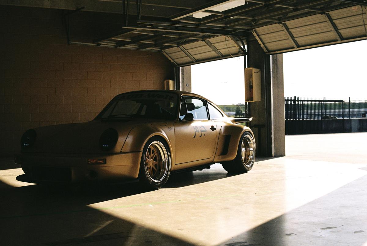 A gold sports car is parked in a garage with the door open, casting shadows on the floor.