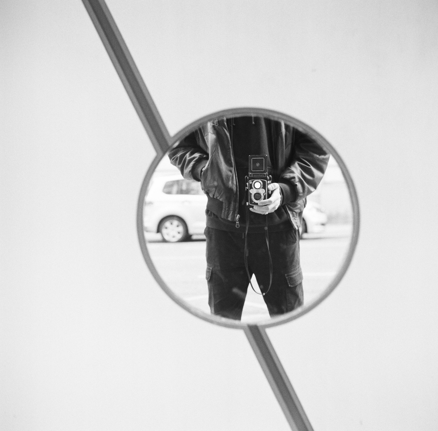 A man holds a camera in his hands, reflected in a circular mirror.