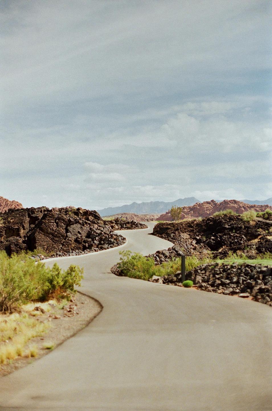 A winding road curves through a rocky, arid landscape under a cloudy sky.