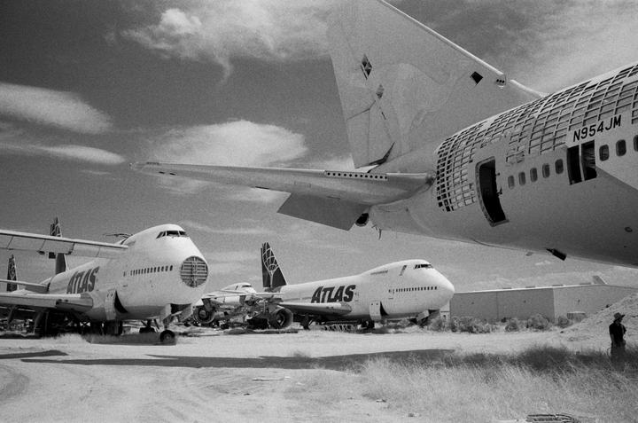Several large airplanes are parked in a desert landscape under a cloudy sky.