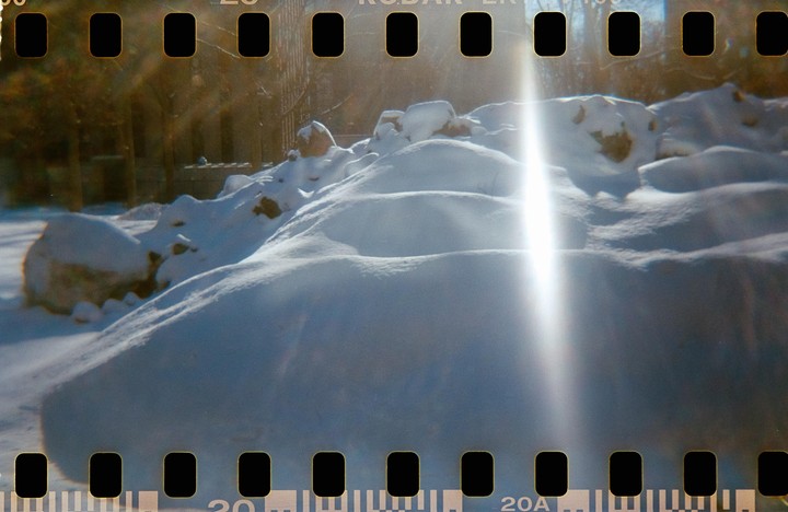 Sunlight creates a strong lens flare over a snow-covered landscape.