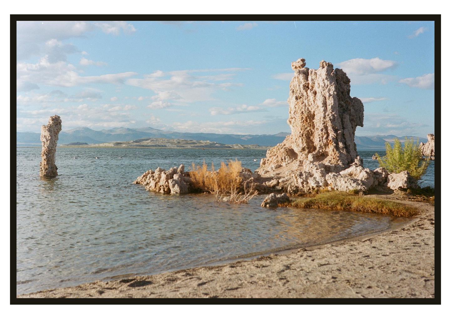 Tufa formations rise from the water and line the shore of Mono Lake under a partly cloudy sky.