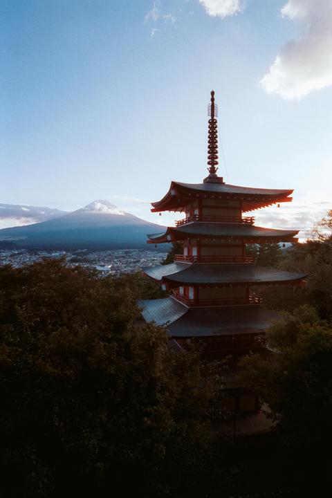 A pagoda stands among trees with a mountain and city in the background under a blue sky.