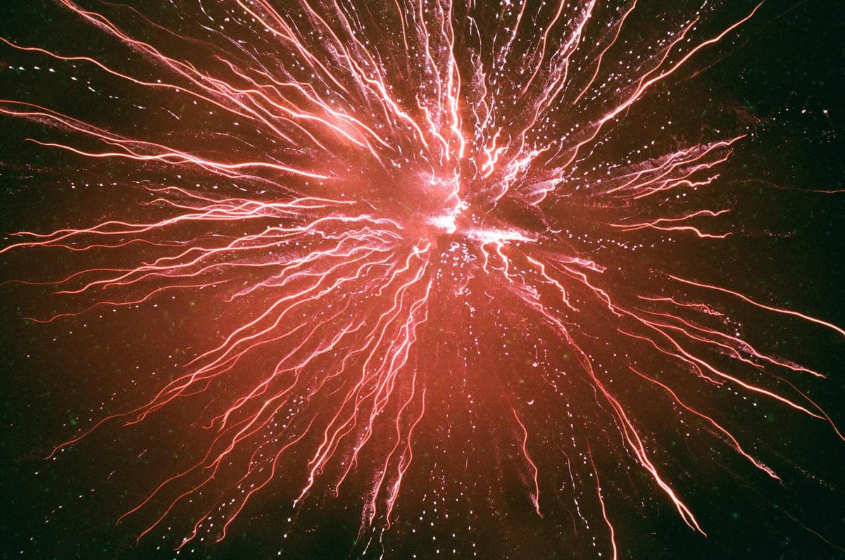 A red firework explodes in the night sky, creating streaks of light.
