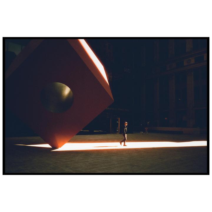 A man walks through a beam of light next to a large red sculpture.