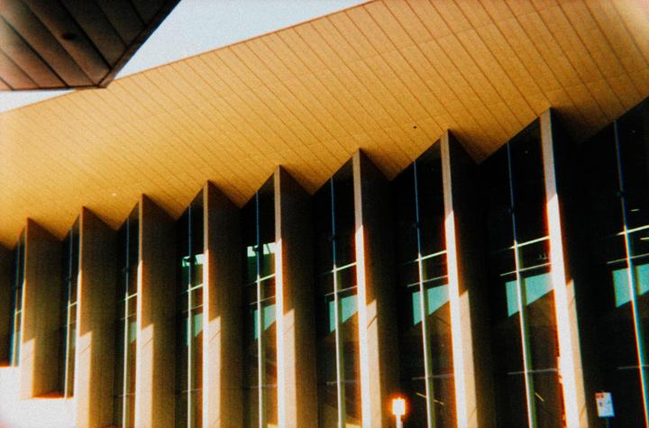 The exterior of a building with a textured ceiling and angular windows is shown from a low angle.