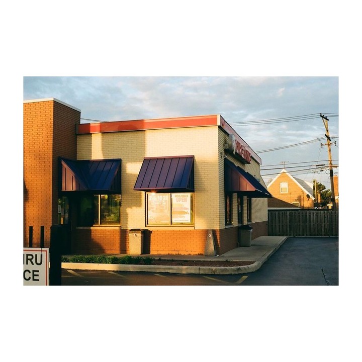 A Burger King restaurant with blue awnings is illuminated by golden hour light.