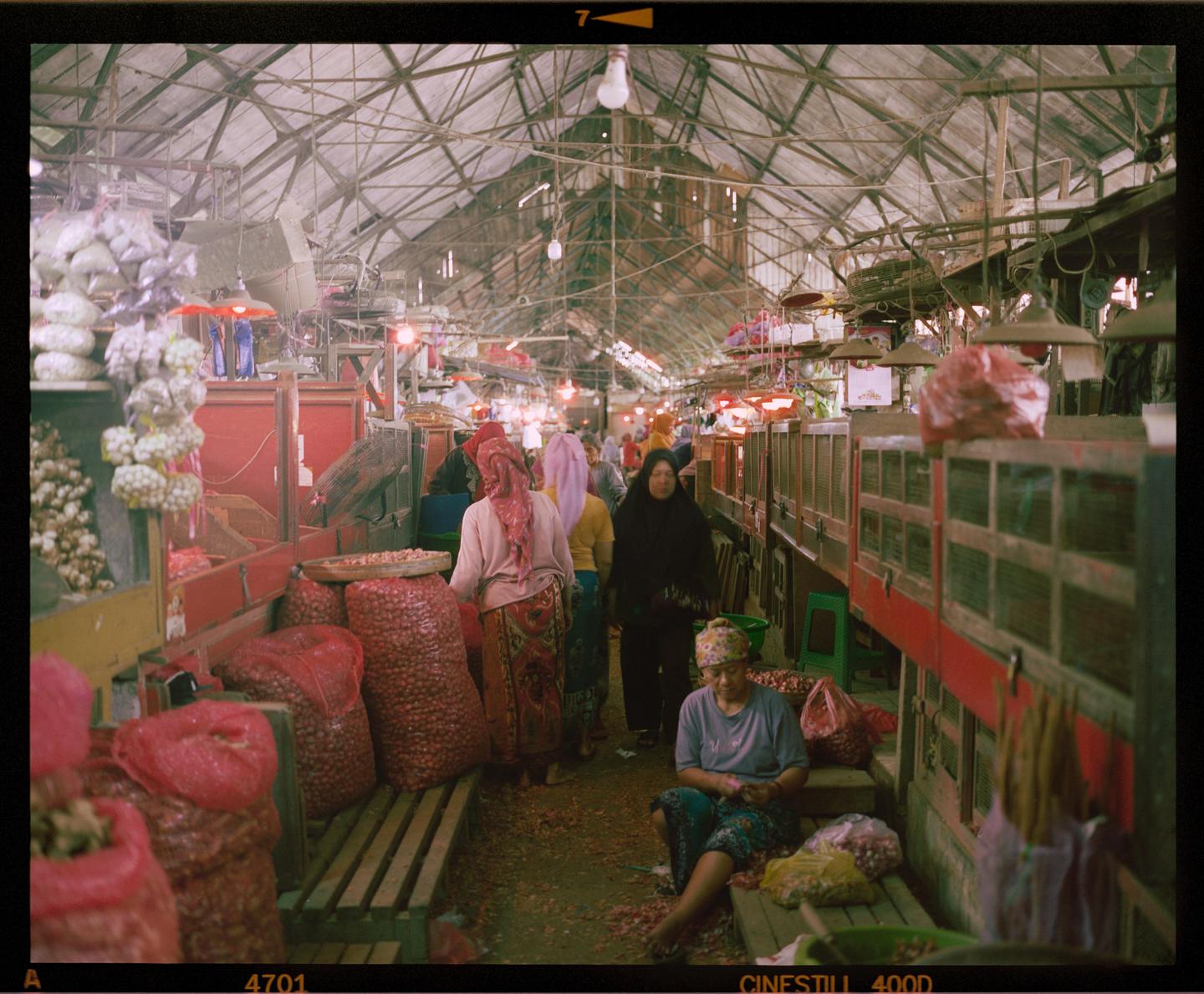 A busy market scene shows people and produce under a high, vaulted ceiling.