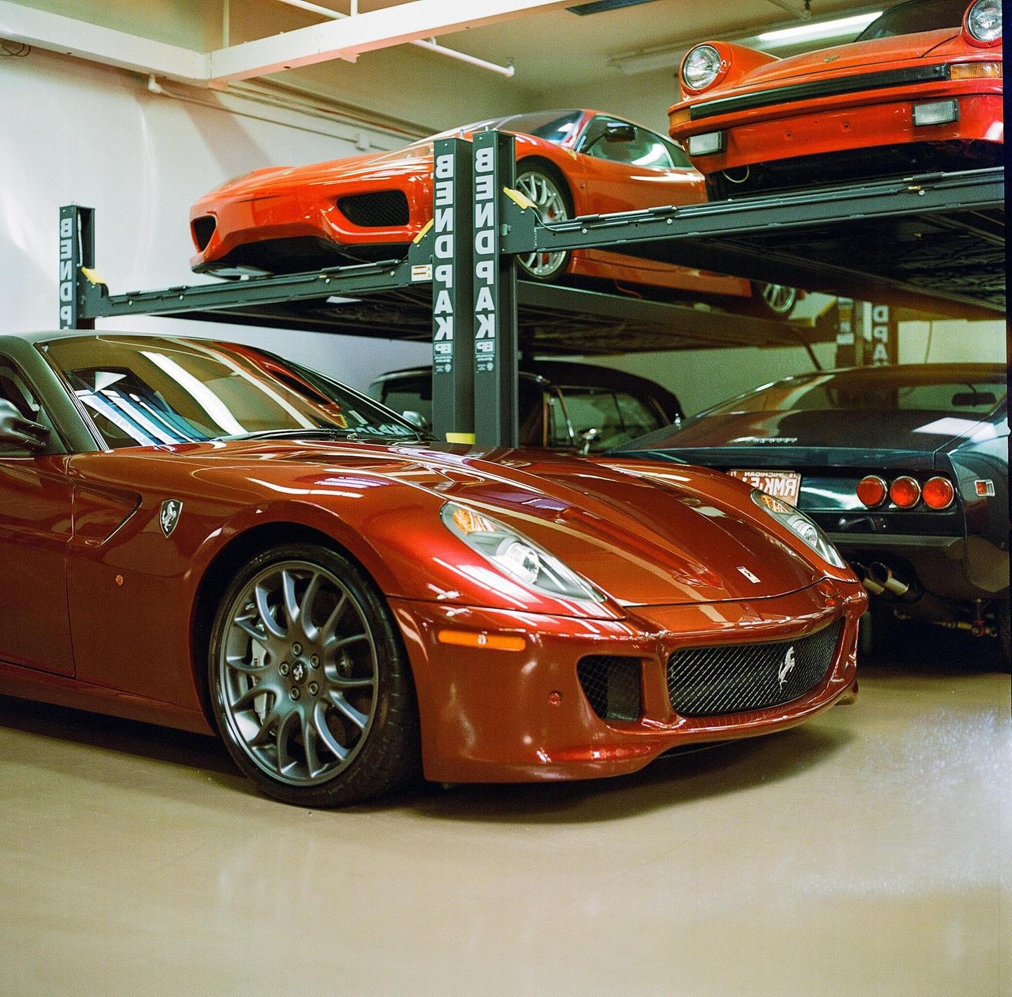Four luxury cars are parked in a garage, with two on a lift and two on the ground.