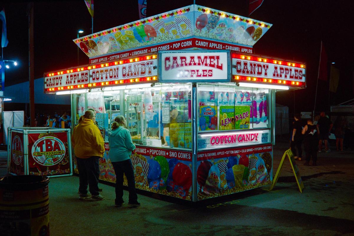 Two people stand in front of a brightly lit concession stand at night.