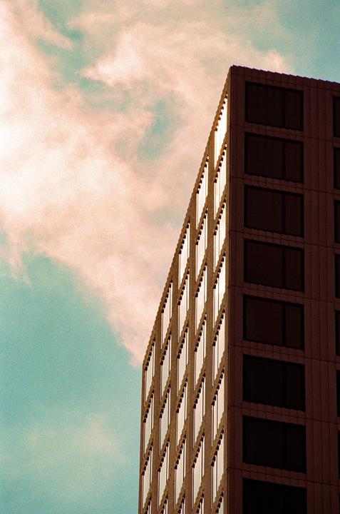 A tall building with many windows is shown against a cloudy sky.