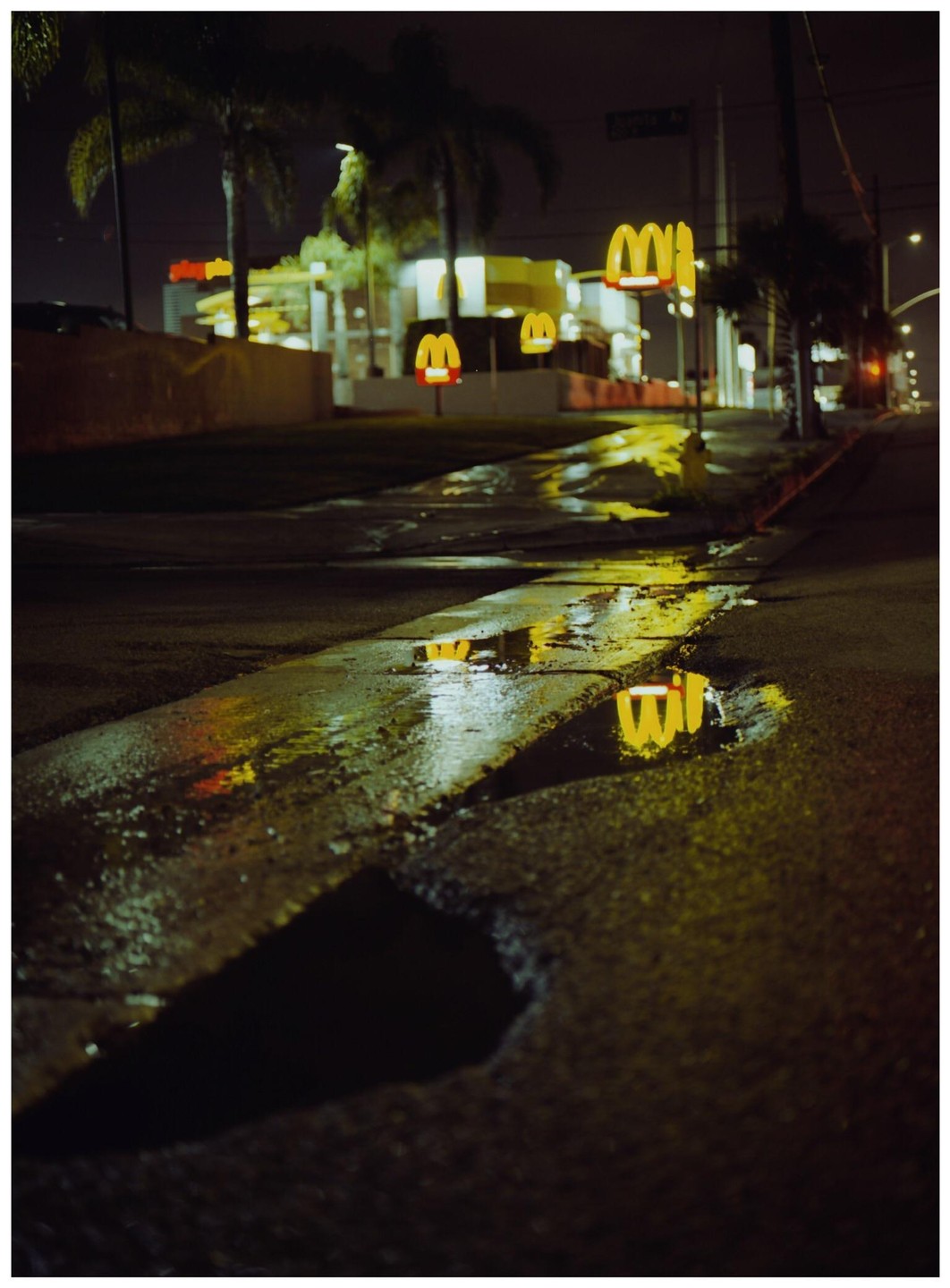 Golden arches from a McDonald's are reflected in puddles on a wet street at night.