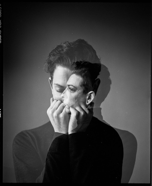 A double exposure shows a man with his eyes closed and his hands near his mouth, overlaid with a profile view of another man's face.