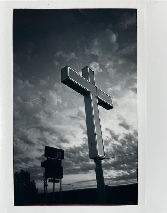A large cross sign stands against a cloudy sky.