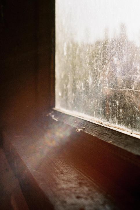 A dirty window and wooden window sill are illuminated by sunlight.