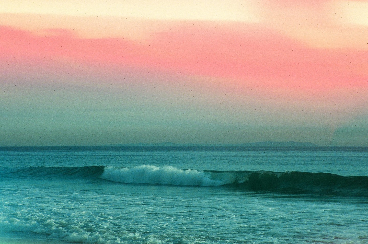 A wave breaks in the ocean under a pastel sky.