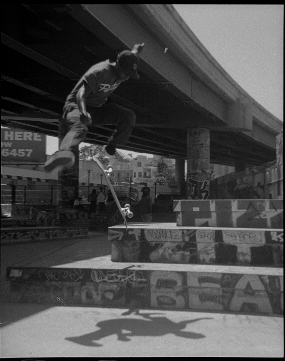 A man jumps on a skateboard over a concrete structure covered in graffiti under a bridge.