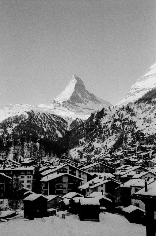 A snow-covered village sits in a valley with a large, jagged mountain peak in the background.