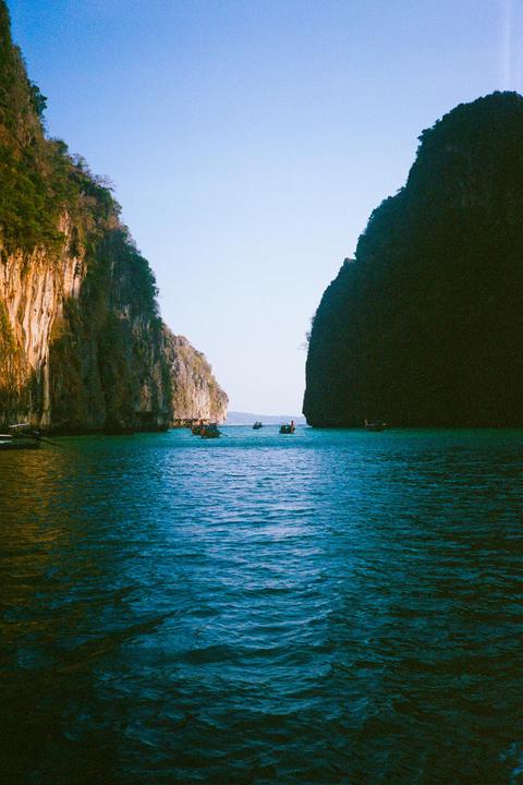 Boats are visible in the water between two large rock formations.