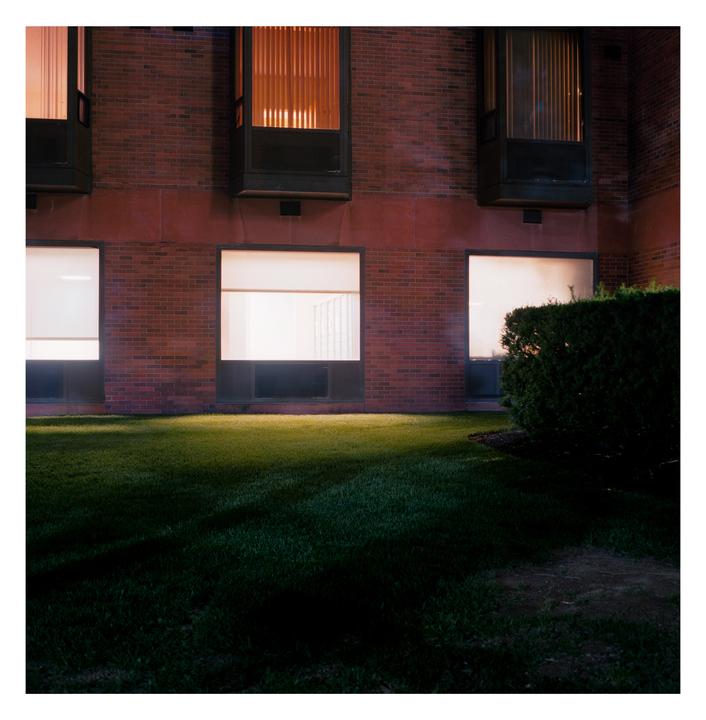 A brick building with illuminated windows overlooks a grassy lawn at night.