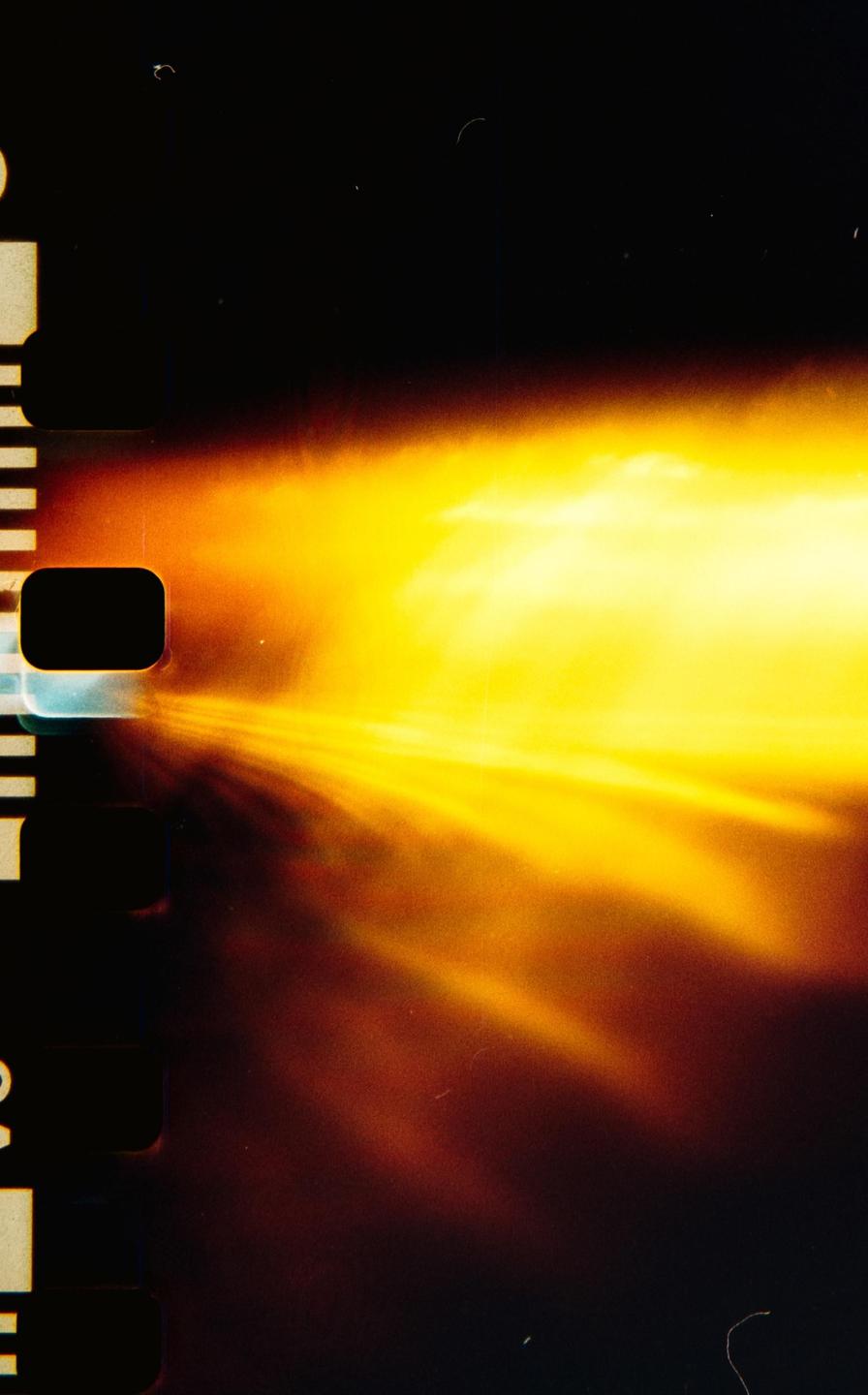 A bright yellow and orange light streak across a dark background with film sprockets visible on the left.