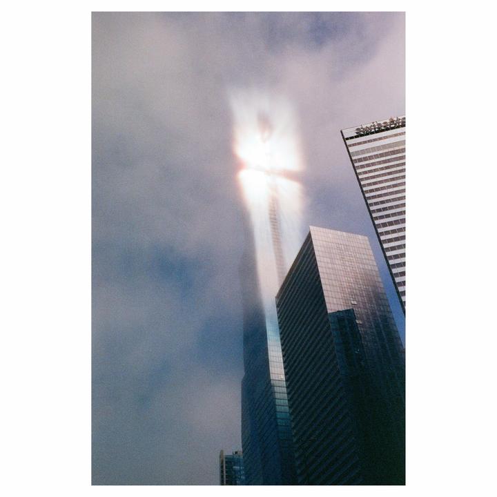 A tall skyscraper is partially obscured by clouds, with a bright light emanating from its upper section.