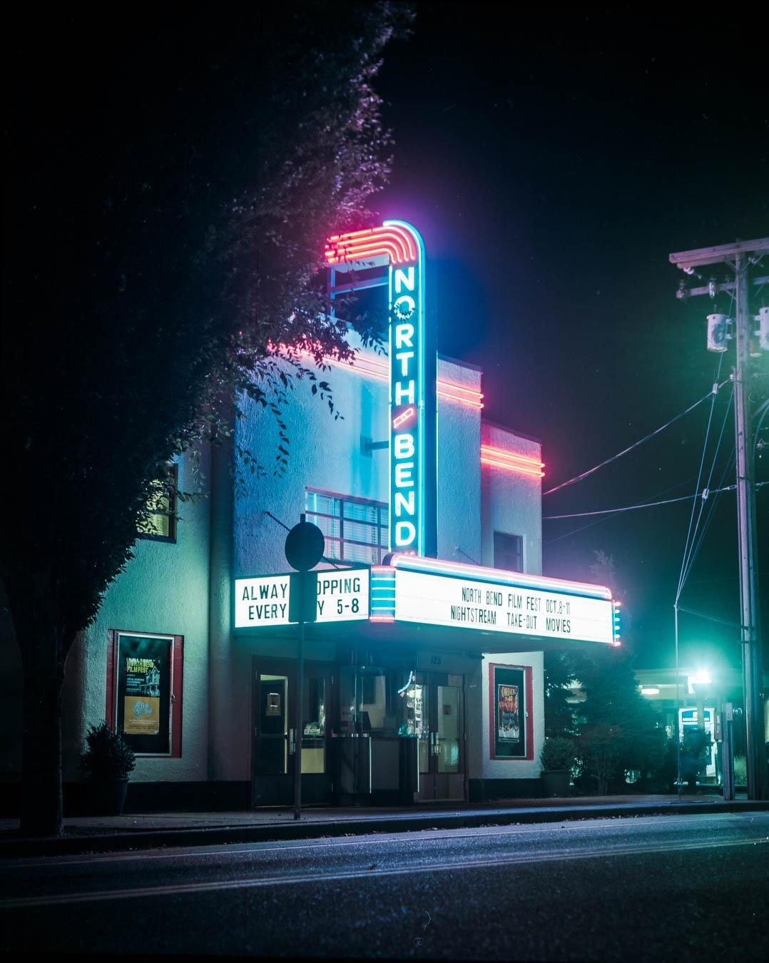 A movie theater with a neon sign that says "North Bend" is illuminated at night.
