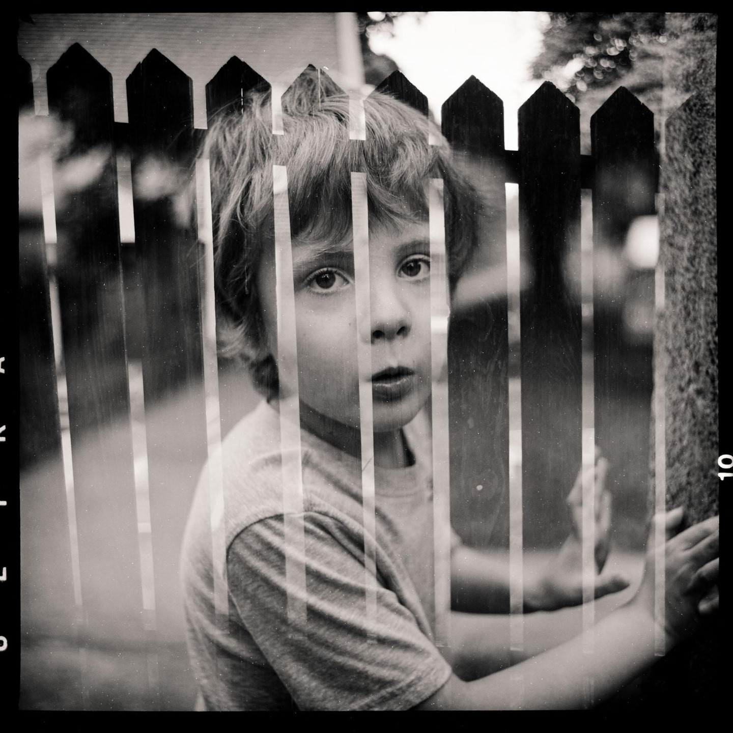 A child with shaggy hair looks through a wooden fence.