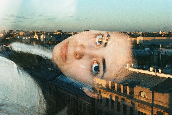 A double exposure shows a woman's face superimposed over a cityscape at sunset.