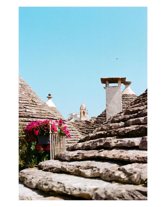 A view of conical stone roofs and a distant bell tower under a clear blue sky.