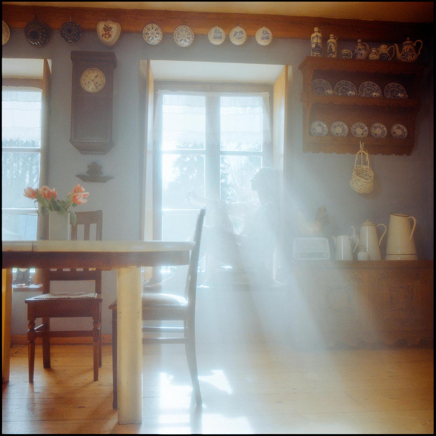 Sunlight streams through a window into a room with a table, chairs, and various decorative items.