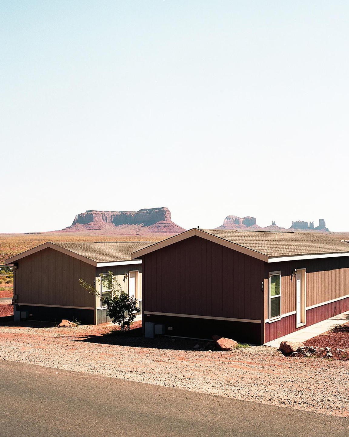 Two houses sit on a gravel lot with large mesas in the background.
