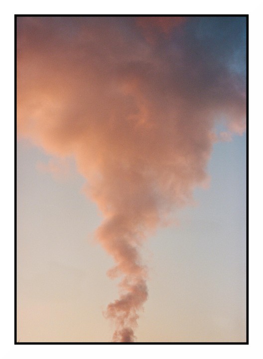 A plume of orange smoke rises into a pale blue sky.