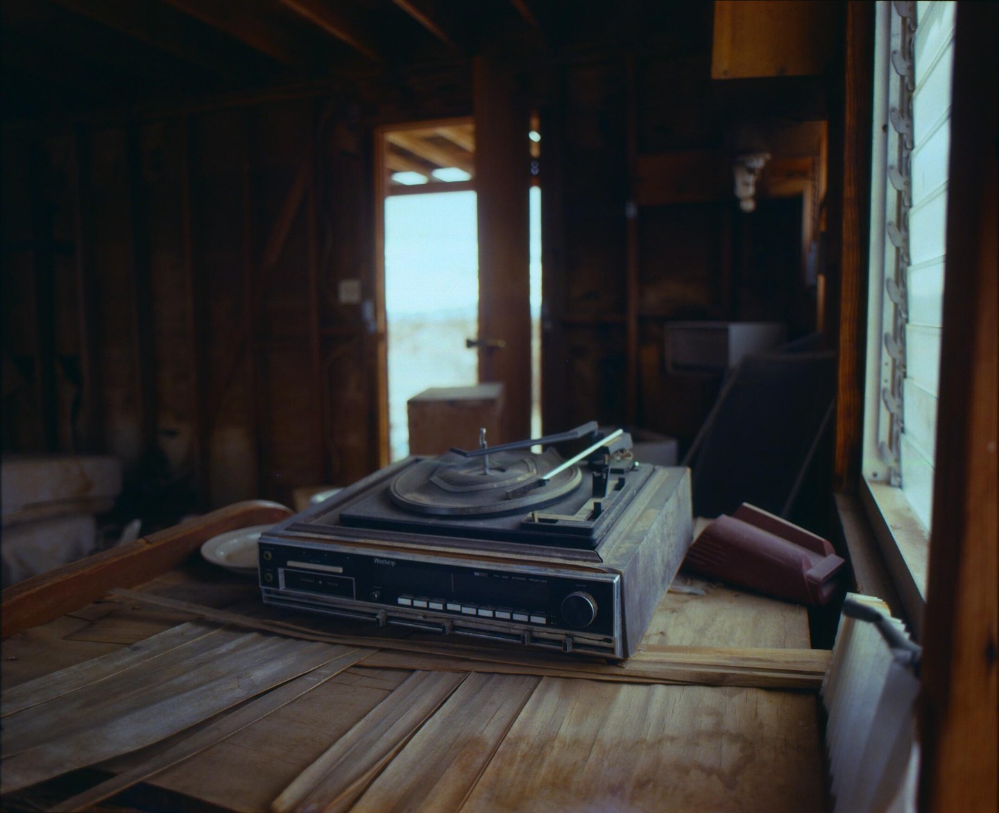 A record player sits on a wooden surface in a dimly lit room with an open doorway and a window.