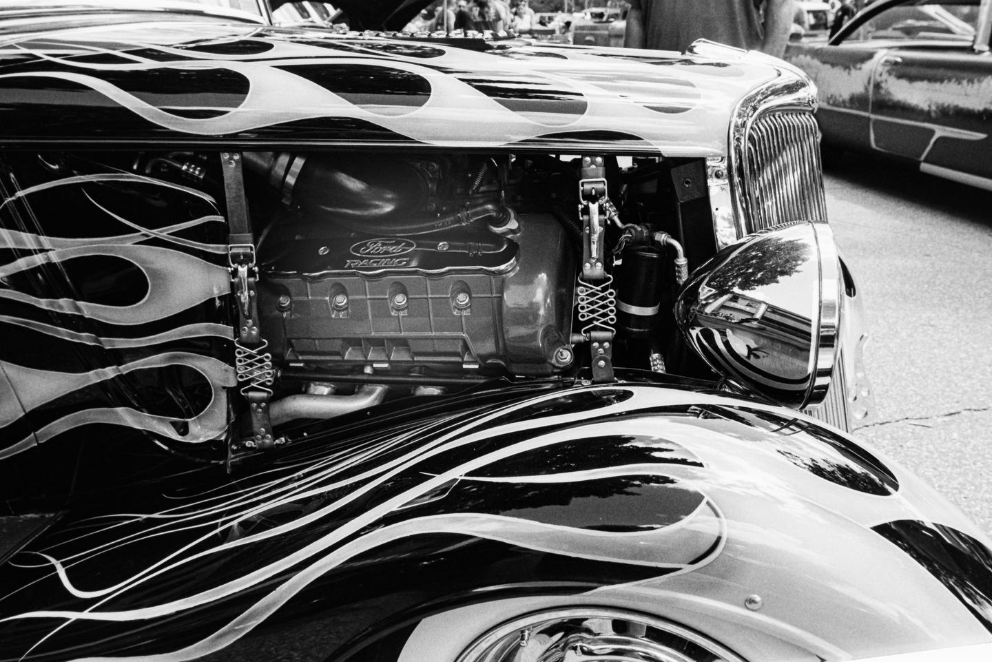 A black and white close-up shows the front of a vintage car with flame decals and a visible engine.